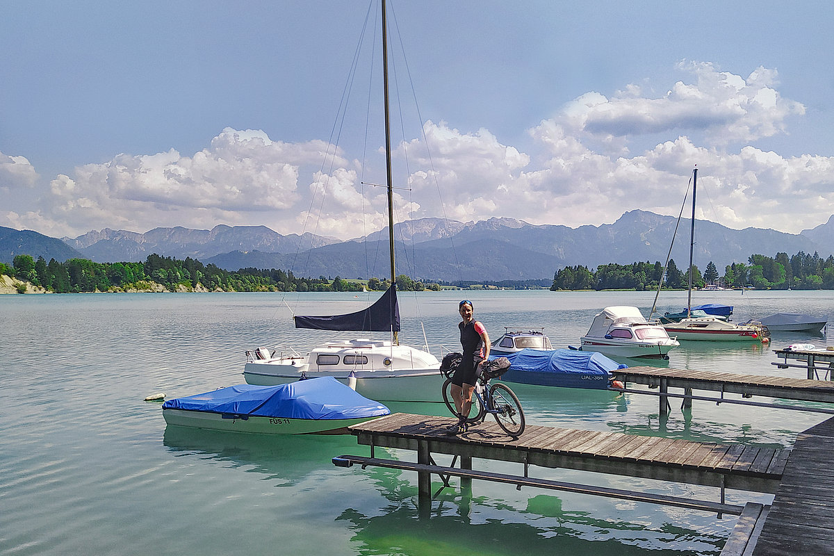 Eine Radfahrerin steht mit ihrem Fahrrad auf einem Steg am Forggensee.