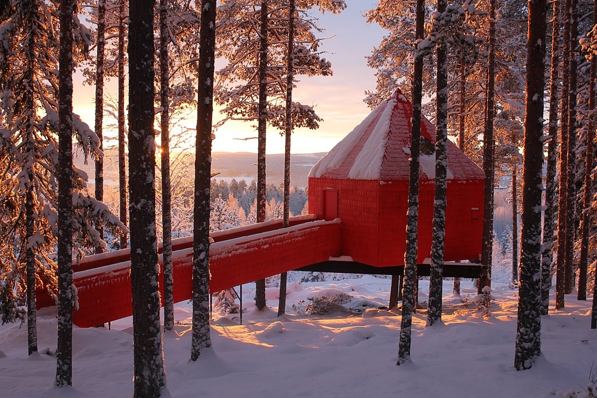 Ein rotes Baumhaus mit Rampe in einem schwedischen Winterwald bei tief stehender Sonne