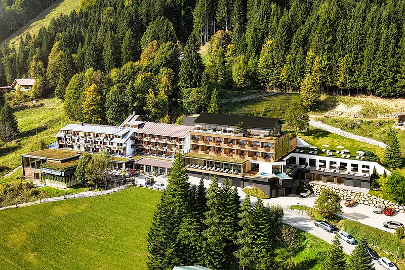 Luftaufnahme eines Hotelkomplexes an einem Wald-Wiesenhang