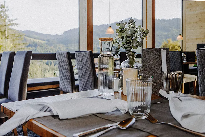 Ansicht eines gedeckten Restauranttisches vor einem großen Fenster mit Blick ins Grüne