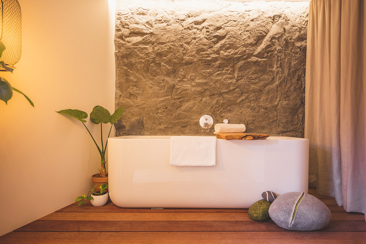 Auf dem Bild sieht man eine Badewanne in einer Zimmernische mit Steinfassade. Drumherum stehen einige Pflanzen und andere Dekoelemente.