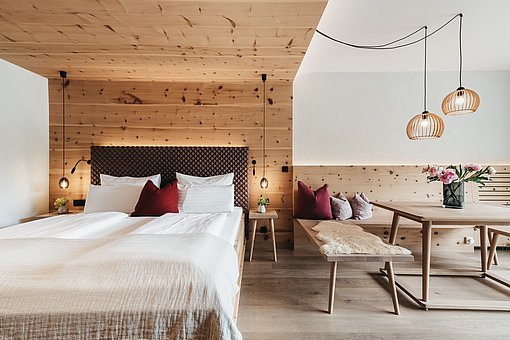 Blick in ein Hoteldoppelzimmer mit Doppelbett und einem Holztisch mit Sitzbank
