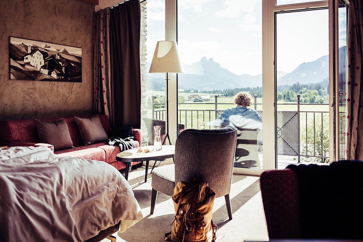 Ein Mann sitzt auf einem Balkon einer Hotelzimmers und schaut in die Berge