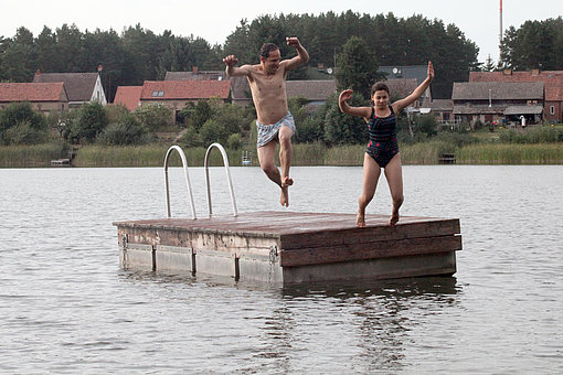 Zwei Personen springen von einem Steg in einen See