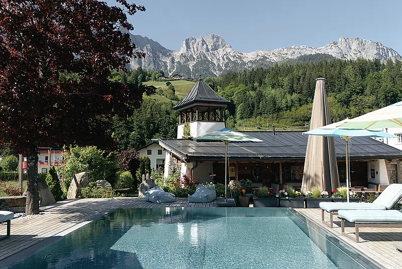 Ansicht Hotelaußenpool mit Liegen und Sonnenschirmen am Rad, im Hintergrund schroffe, felsige Berggipfel