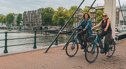 Zwei Frauen radeln über eine Grachtenbrücke