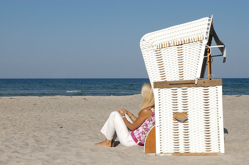 Eine Frau sitzt vor einem Standkorb am Strand