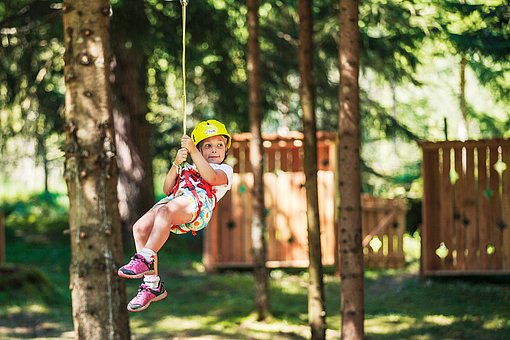 Mädchen mit Helm hängt in einem Seilgurtsystem an einem Baum