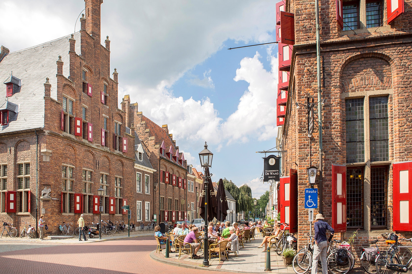 Straße mit alten Backsteinhäusern im holländischen Stil, Gastronomie mit Außentischen und vielen Gästen und Gästinnen