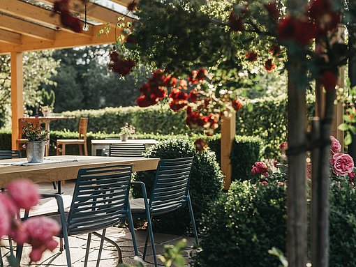 Blick auf eine Terrasse mit Tischen und Stühlen unter einer Pergola