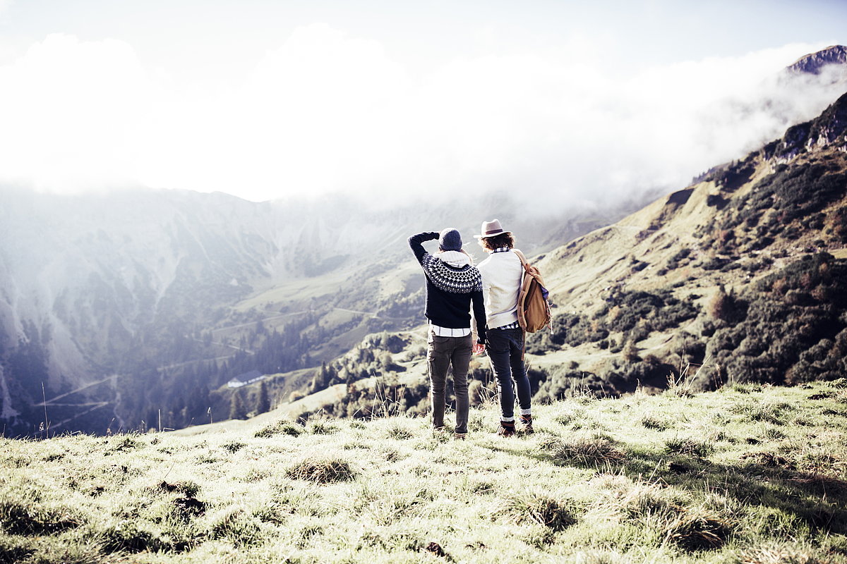 Zwei Menschen stehen mitten in der Natur und schauen in die ferne Bergwelt