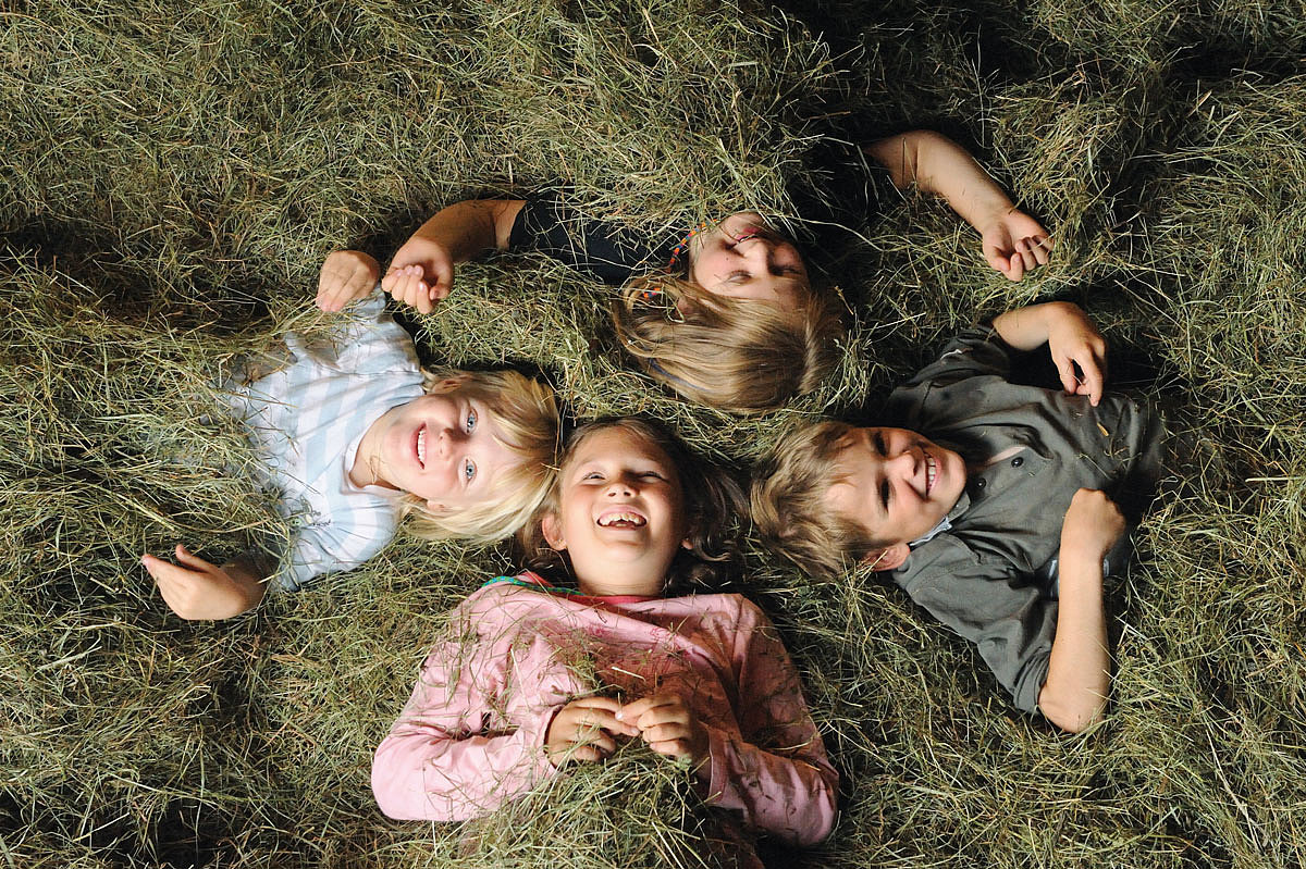 Vier Kinder liegen im Kreis im Heu und lachen in die Kamera