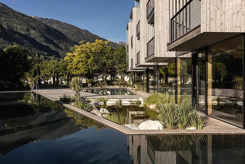 Sommeransicht einer Hotelfassade mit Garten, Terrasse und Pool