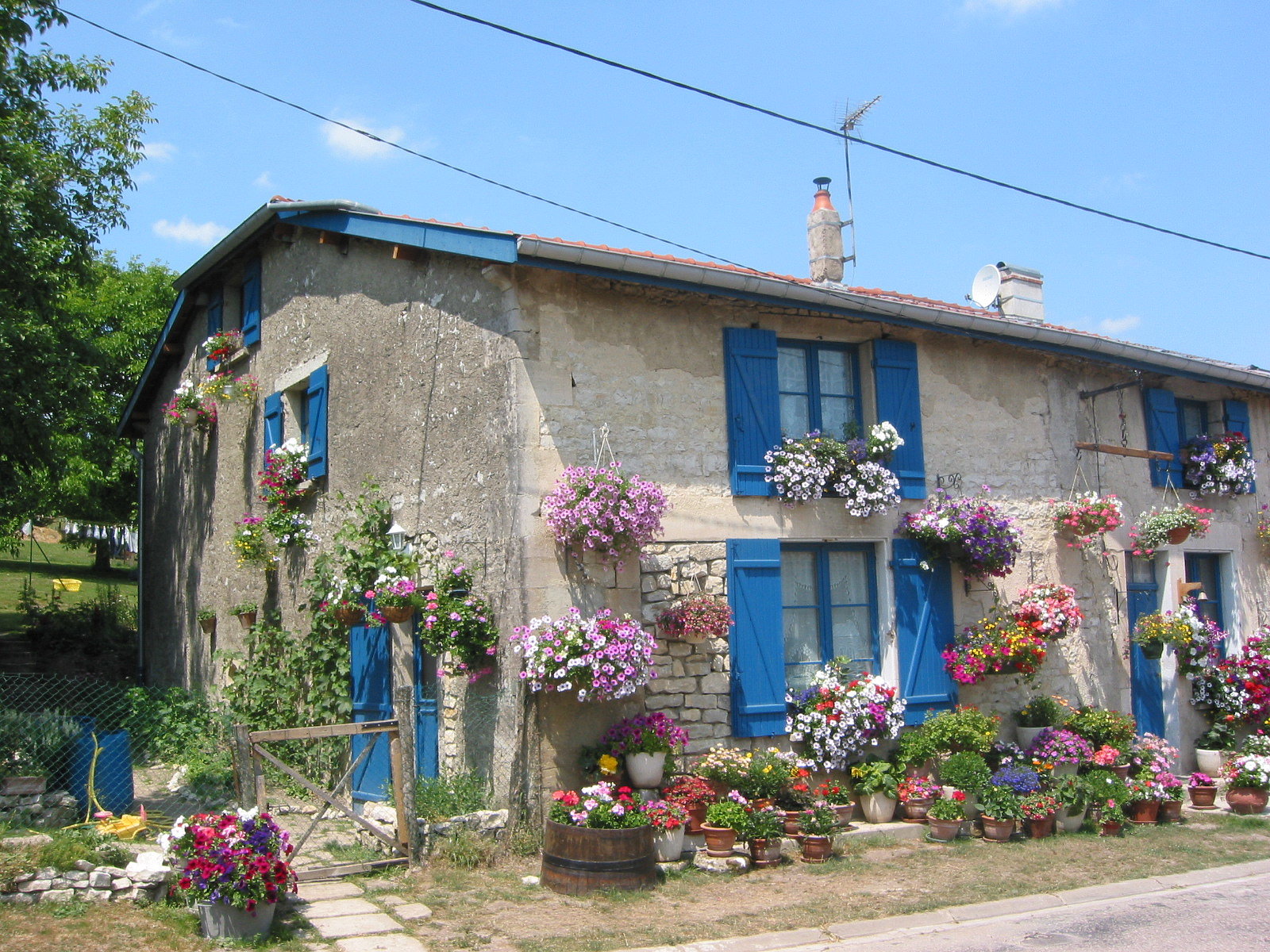 Altes Gebäude aus Stein mit blauen Klappläden und vielen Blumen
