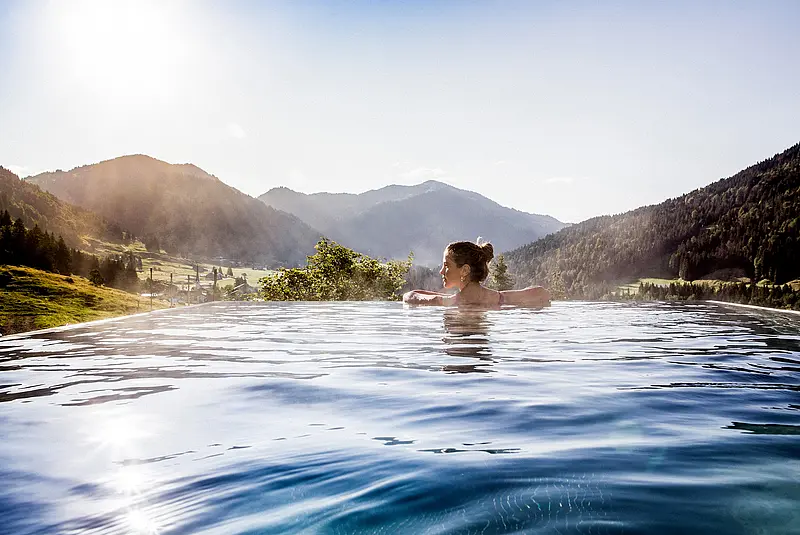Eine Frau schwimmt allein in einem Außenpool mit Blick auf bewaldete Berge