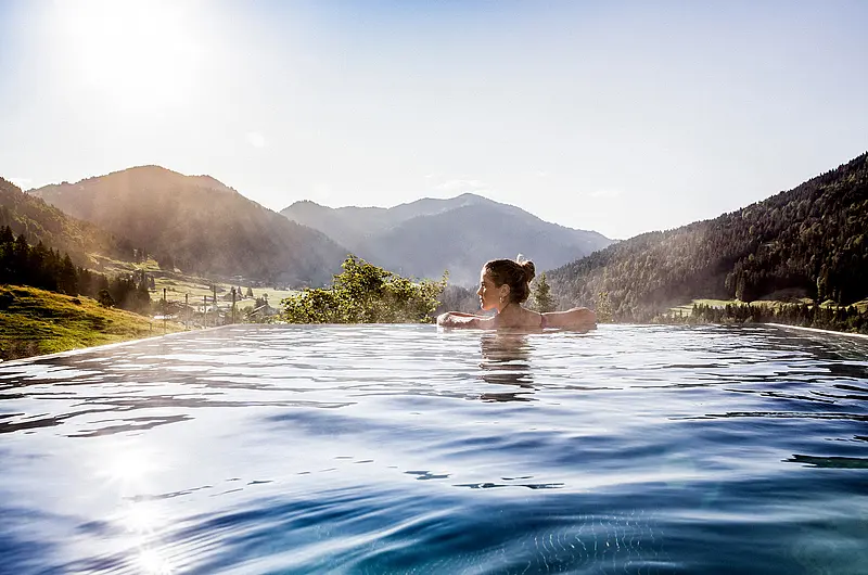 Eine Frau schwimmt allein in einem Außenpool mit Blick auf bewaldete Berge