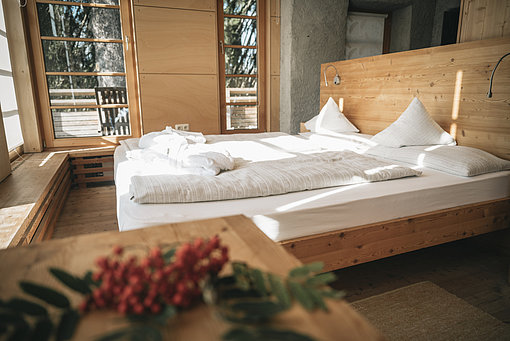 Ein Hotelzimmer mit Doppelbett aus Holz, großen Fenstern und Zugang zu einem Balkon.