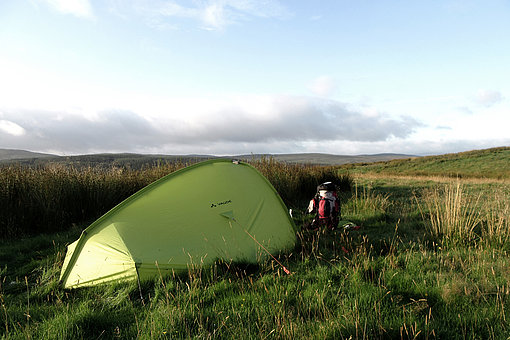 Ein grünes Zelt steht inmitten wilder Landschaft.