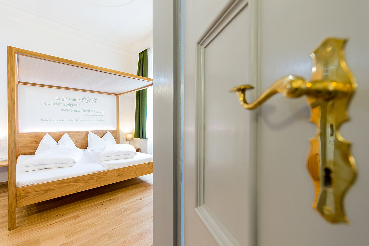 Blick in ein helles Hotelzimmr mit Holzboden und schlichtem Himmelbett