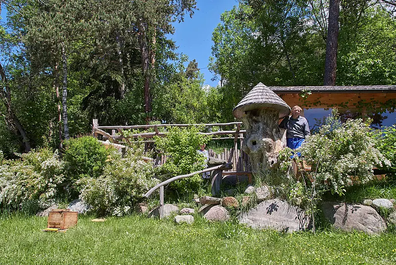 Blick in einen Garten mit Rasen, Findlingen, Büschen, Bäumen und einem Bienenstock