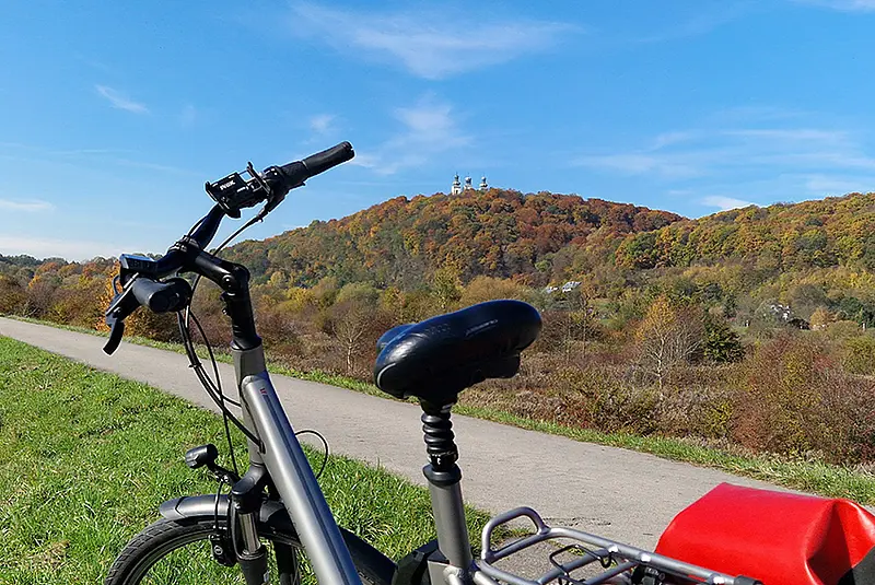 Fahrrad neben einem Radweg vor bewaldeten Hügeln und Wiesen