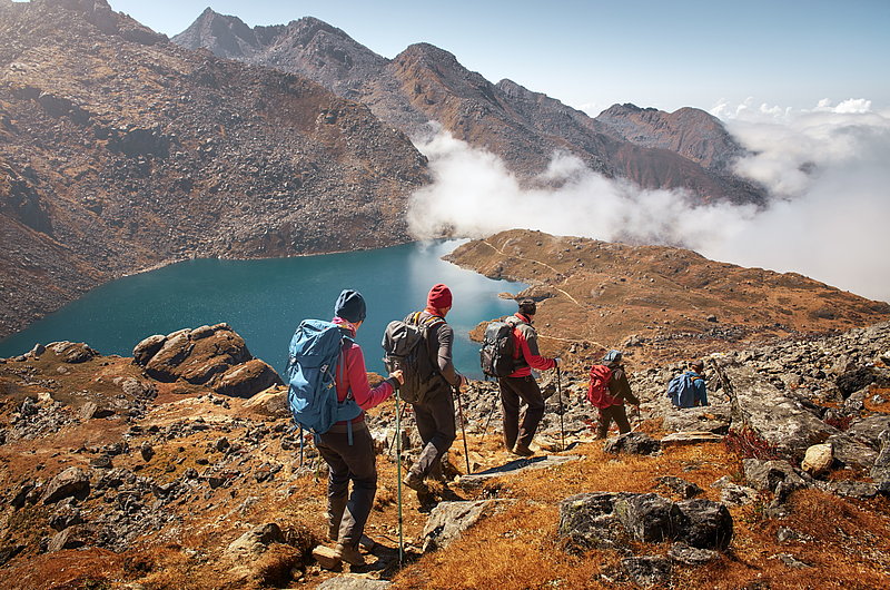 vier Wanderer auf einem felsigen Bergpfad oberhalb eines Bergsees