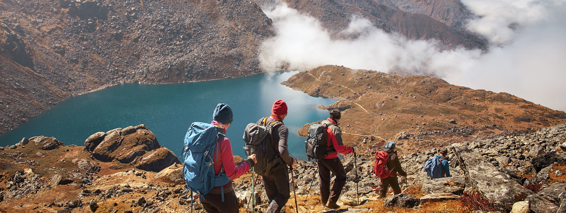 vier Wanderer auf einem felsigen Bergpfad oberhalb eines Bergsees