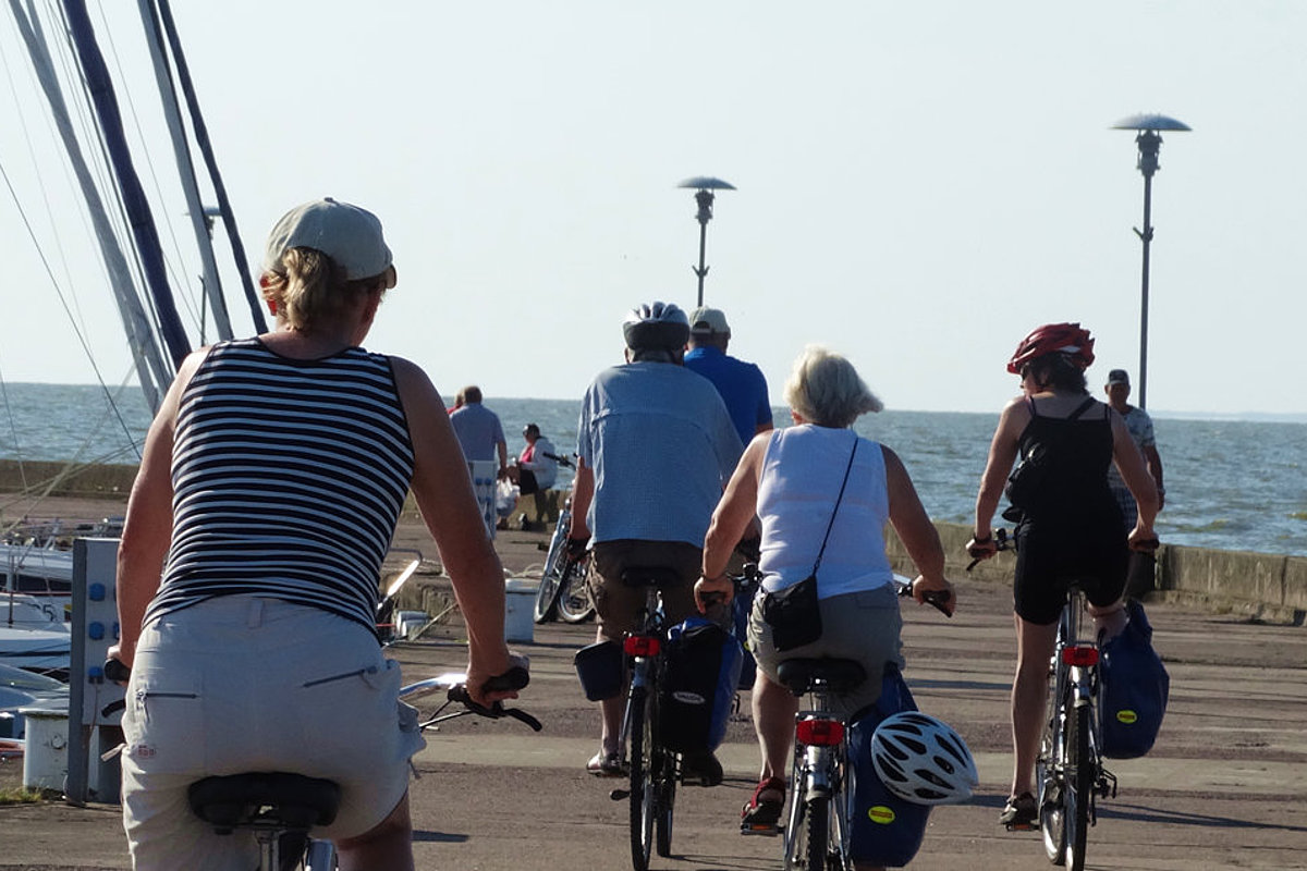 Viele Radfahrende fahren auf einem Steg entlang der Küste.