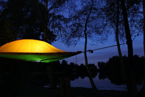 Ein leuchtendes, an zwei Bäumen aufgehängtes Zelt in der Nacht