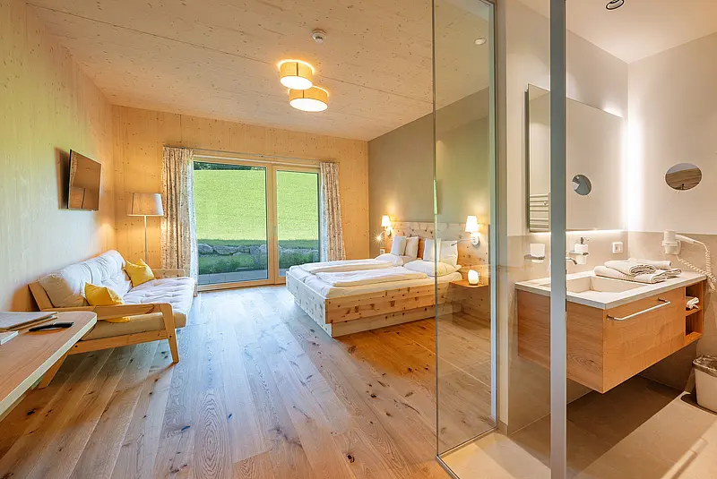 Innenansicht eines weitäufigen Hoteldoppelzimmers mit Holzmöblen und Holzfußboden