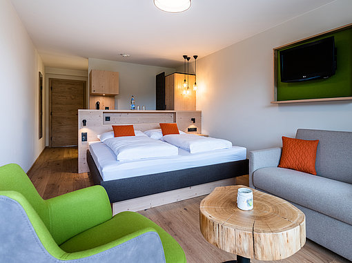 Innenansicht Hoteldoppelzimmer mit Doppelbett, Sitzecke und Couchtisch mit einer Tischplatte aus einer großen runden Baumscheibe