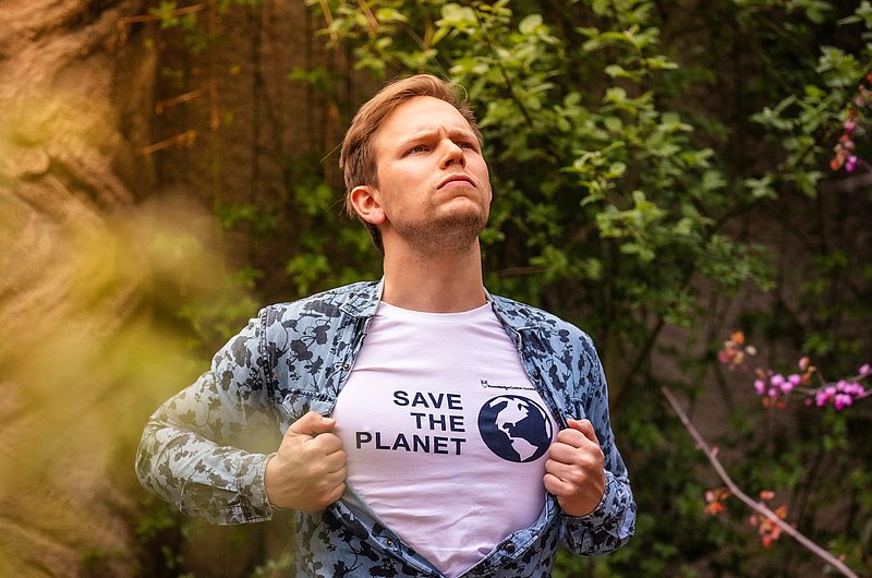 Ein Mann öffnet sein Hemd und zeigt das T-Shirt darunter mit der Beschriftung "Save the planet"