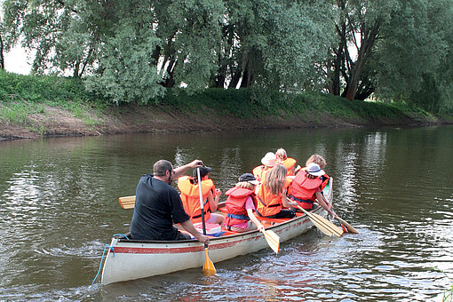 Ein Erwachsener und mehrere Kinder mit Schwimmwesten paddeln in einem Kanu