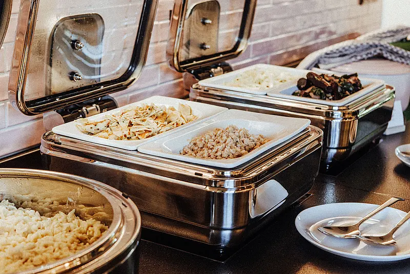 Ansicht eines Buffets mit aufgeklappten Warmhaltebehältern und verschiedenen warmen Speisen darin