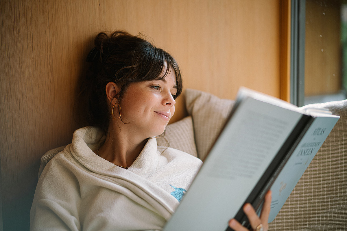 Eine Frau sitzt im Bademantel und liest in einem Buch