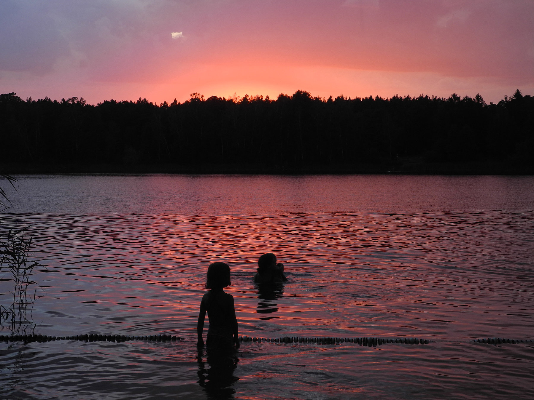 Ein See bei Sonnenuntergang mit der Silhouette eines Mädchens im Vordergrund