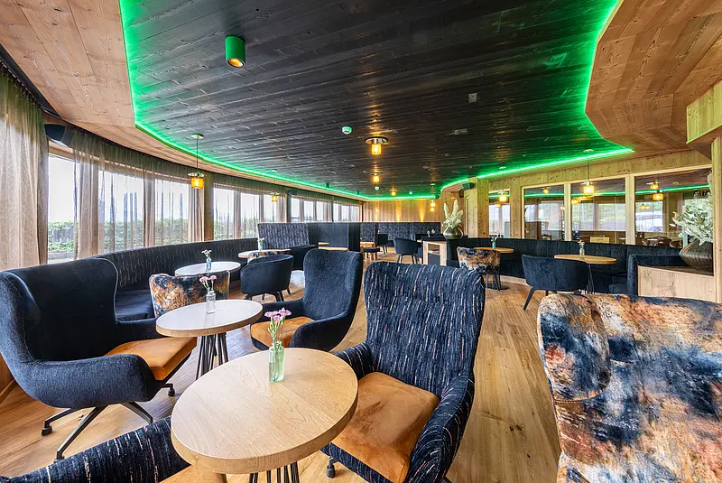 Innenansicht einer Hotellobby mit Sesseln um kleine runde Tische mit Fenstern bis zum Boden