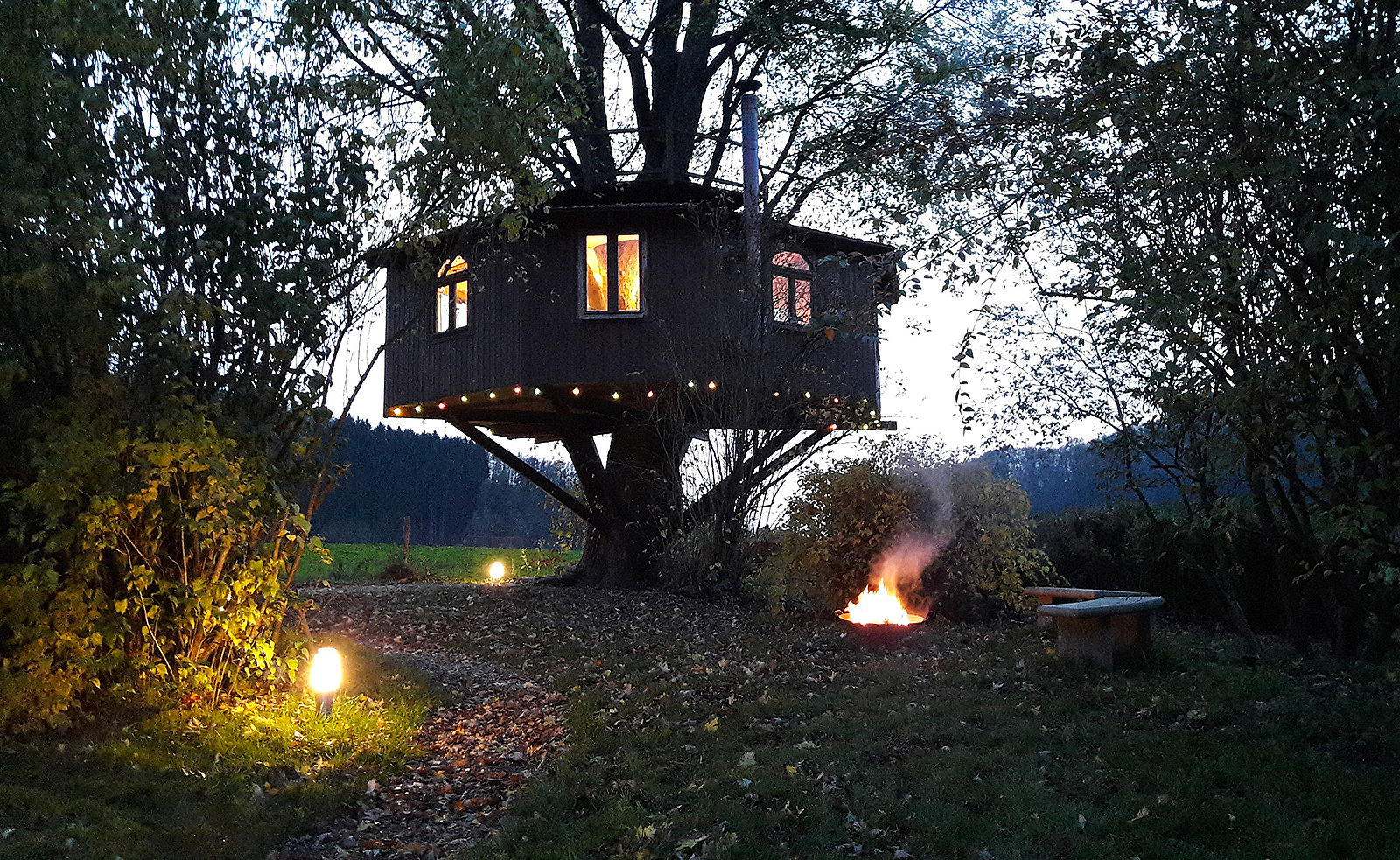 Ein Baumhaus in der Abenddämmerung neben einer Feuerstelle