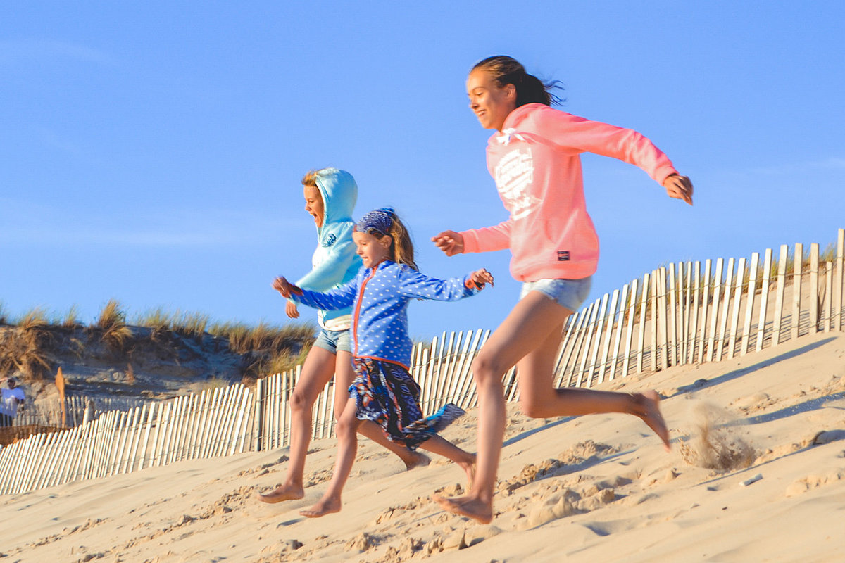 Drei Kinder laufen eine Düne auf Sand herunter.