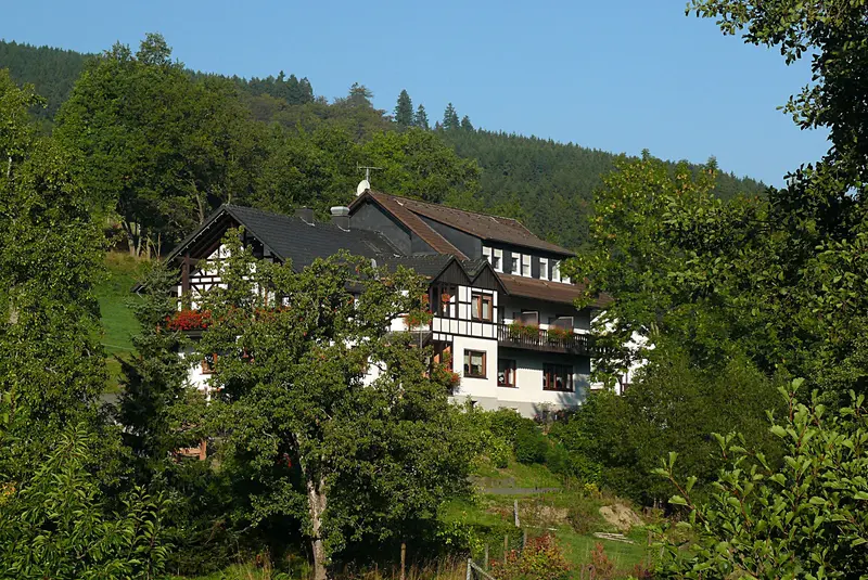 Fachwerkhaus zwischen Obstbäumen mit bewaldeten Hügeln im Hintergrund