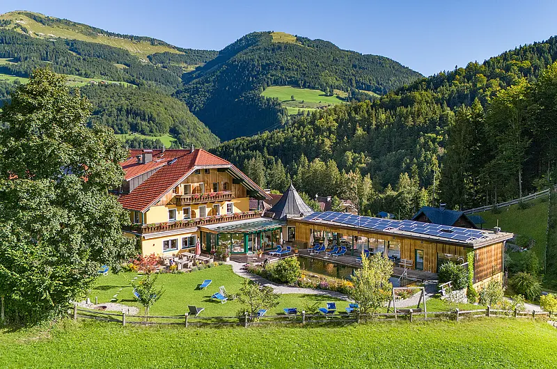 Ansicht eines Hotels umgeben von Wiesen und bewaldeten Hügeln