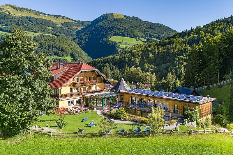 Ansicht eines Hotels umgeben von Wiesen und bewaldeten Hügeln