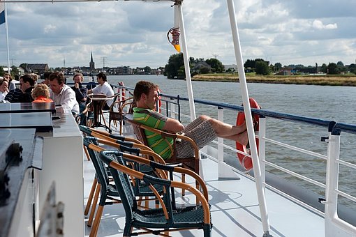 Menschen sitzen auf dem Deck eines Flussschiffs auf Stühlen in der Sonne