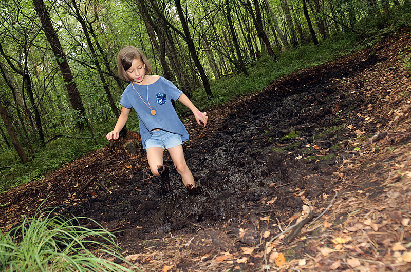 Ein Mädchen springt im Wald in eine Schlammpfütze