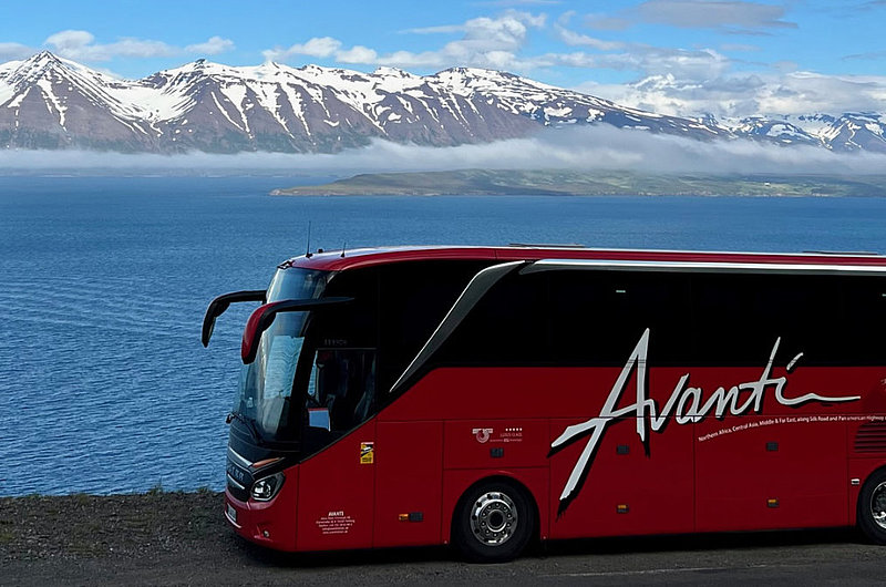 Roter Bus vor dem Meer, im Hintergrund Berge mit Schnee