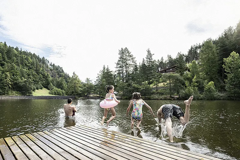 Drei Kinder springen von einem Holzpodest in einen Waldsee