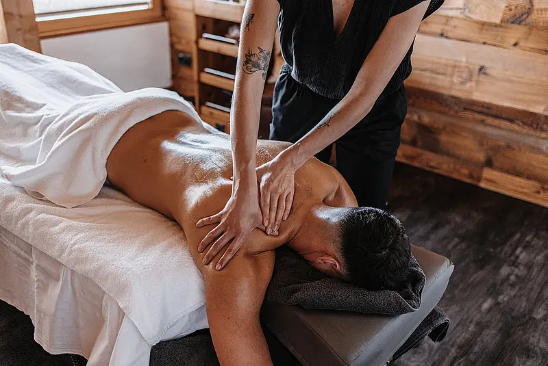 Ein Mann liegt auf dem Bauch auf einer Massageliege und wird von einer Frau im Schulterbereich massiert