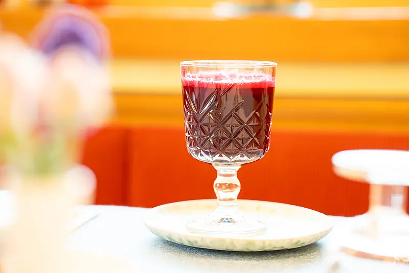 Ein Glas gefüllt mit rotem Saft steht auf einem Tisch auf einem Unterteller aus Porzellan