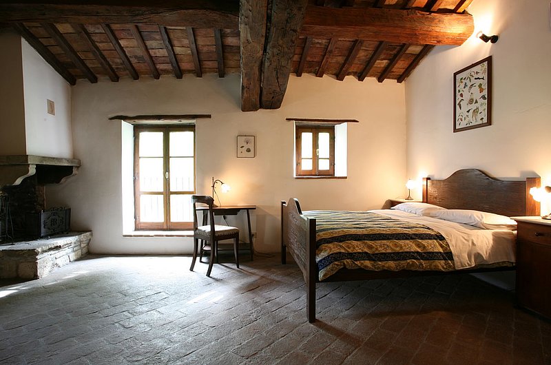 Ein altes, aber gepflegtes Bauernhauszimmer mit Bett, Tisch, Kamin, Holzdecke und einem Fenster