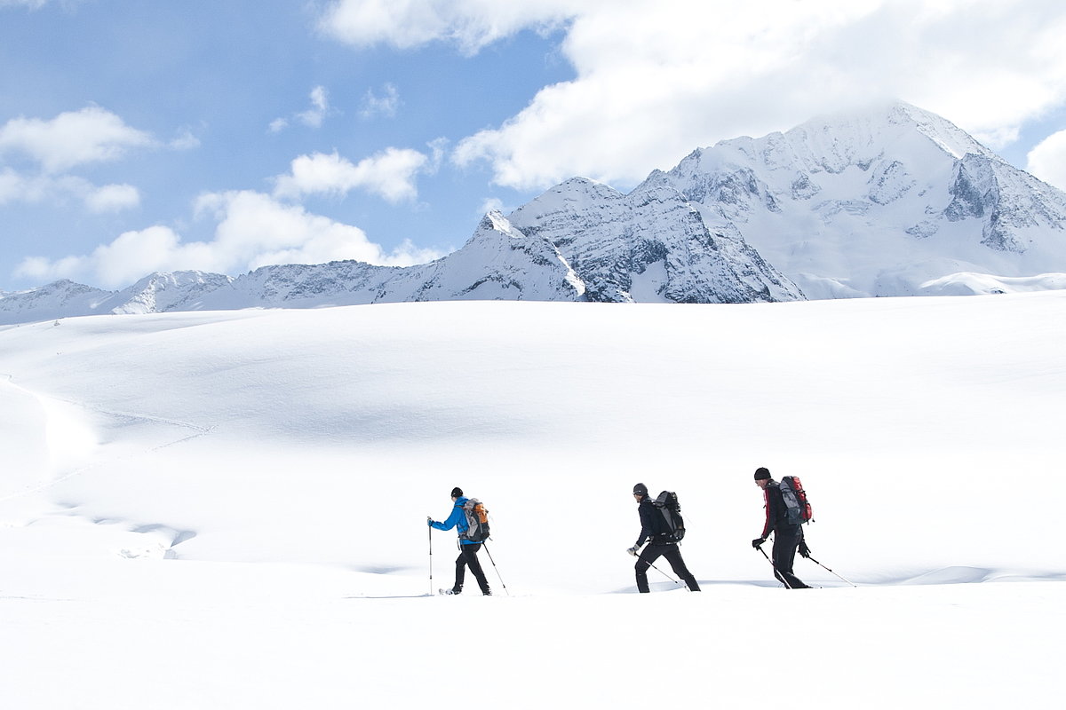 Drei Wanderer in einer weiten Schneelandschaft mit Bergen